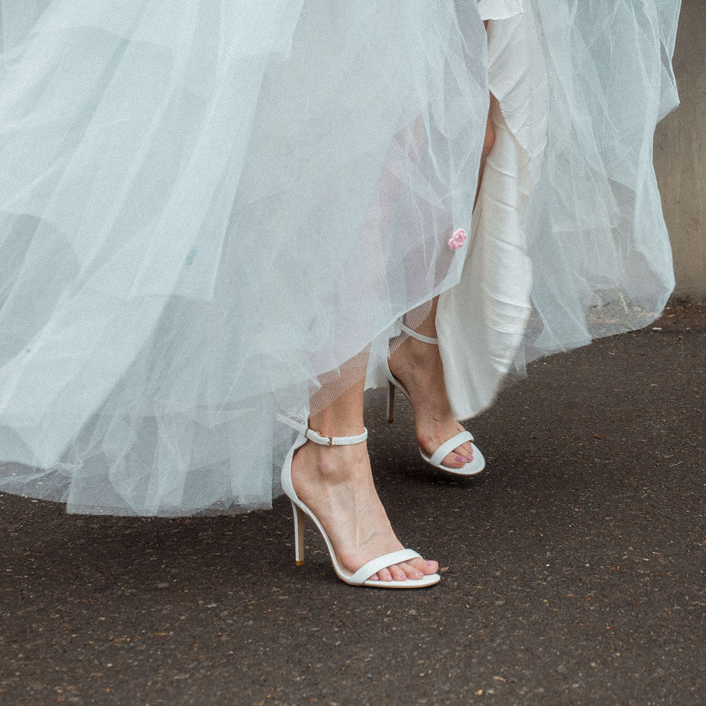 White high-heeled vegan sandals, featuring a minimalist ankle strap design and stiletto heel - stylish women's vegan shoe for an elegant bridal and special occasion look.